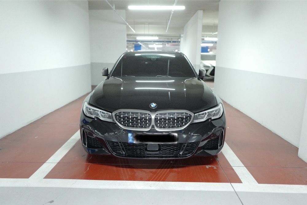 지하주차장 주차칸 안에 정중앙으로 주차된 검은색 BMW M340i 차량의 정면 모습.