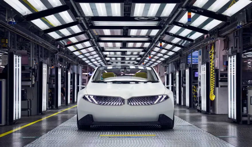 미래형 자동차 공장의 최첨단 자동화 생산 라인 위에서 조립 중인 하얀색 BMW 차량의 정면 모습.