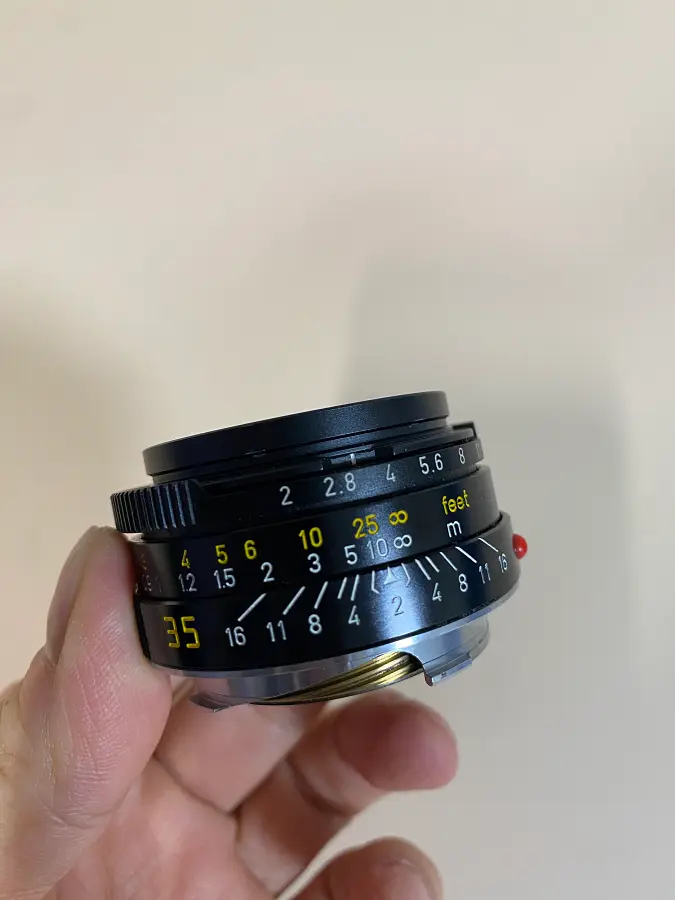 한 손에 들려 있는 작고 검은색의 라이카 35mm 주미크론 4세대 렌즈. 렌즈 경통에 초점 조절을 위한 반달 모양의 포커싱 탭이 달려있다.