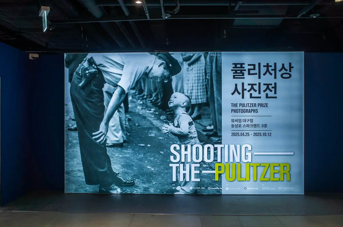 뮤씨엄 대구에 전시된 퓰리처상 사진전 'Shooting the Pulitzer' 공식 포스터. 군복을 입은 남성과 어린아이가 마주 보는 상징적인 흑백 사진이 인상적이다.
