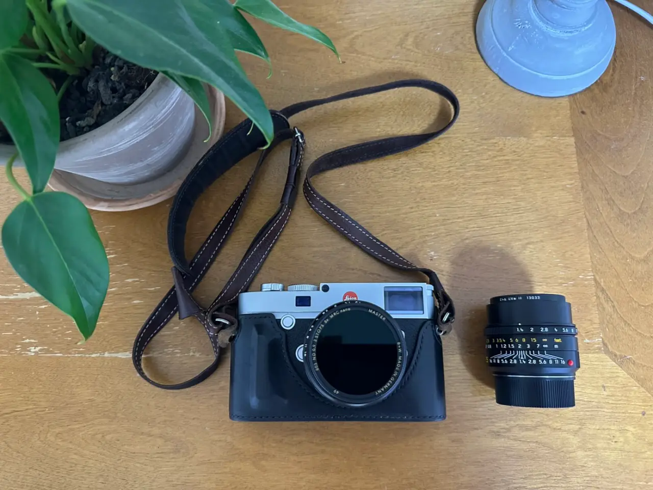 테이블 위에 놓인 실버 색상의 라이카 M10-R 카메라. 카메라에는 50mm 녹티룩스 복각 렌즈가 마운트되어 있고, 그 옆에는 35mm 주미룩스 렌즈가 놓여있다.