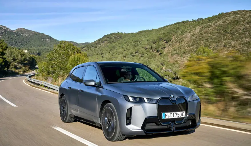 푸른 하늘 아래 도로를 주행하는 BMW iX 전기 SUV. 2024년 고급차 판매 순위 1위를 기록한 BMW의 대표적인 전동화 모델.