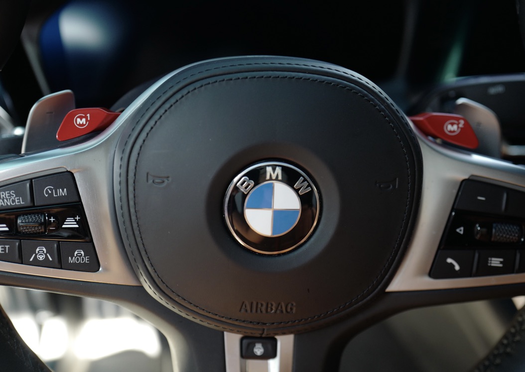 붉은색 M1, M2 버튼이 눈에 띄는 BMW M340i M 스포츠 스티어링 휠 클로즈업 사진.