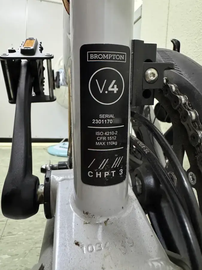브롬톤 자전거 프레임에 부착된 시리얼 넘버 스티커 클로즈업. 'BROMPTON V.4' 로고와 'SERIAL 2301170***' 고유 번호, 'CHPT3' 문구가 선명하게 보인다.