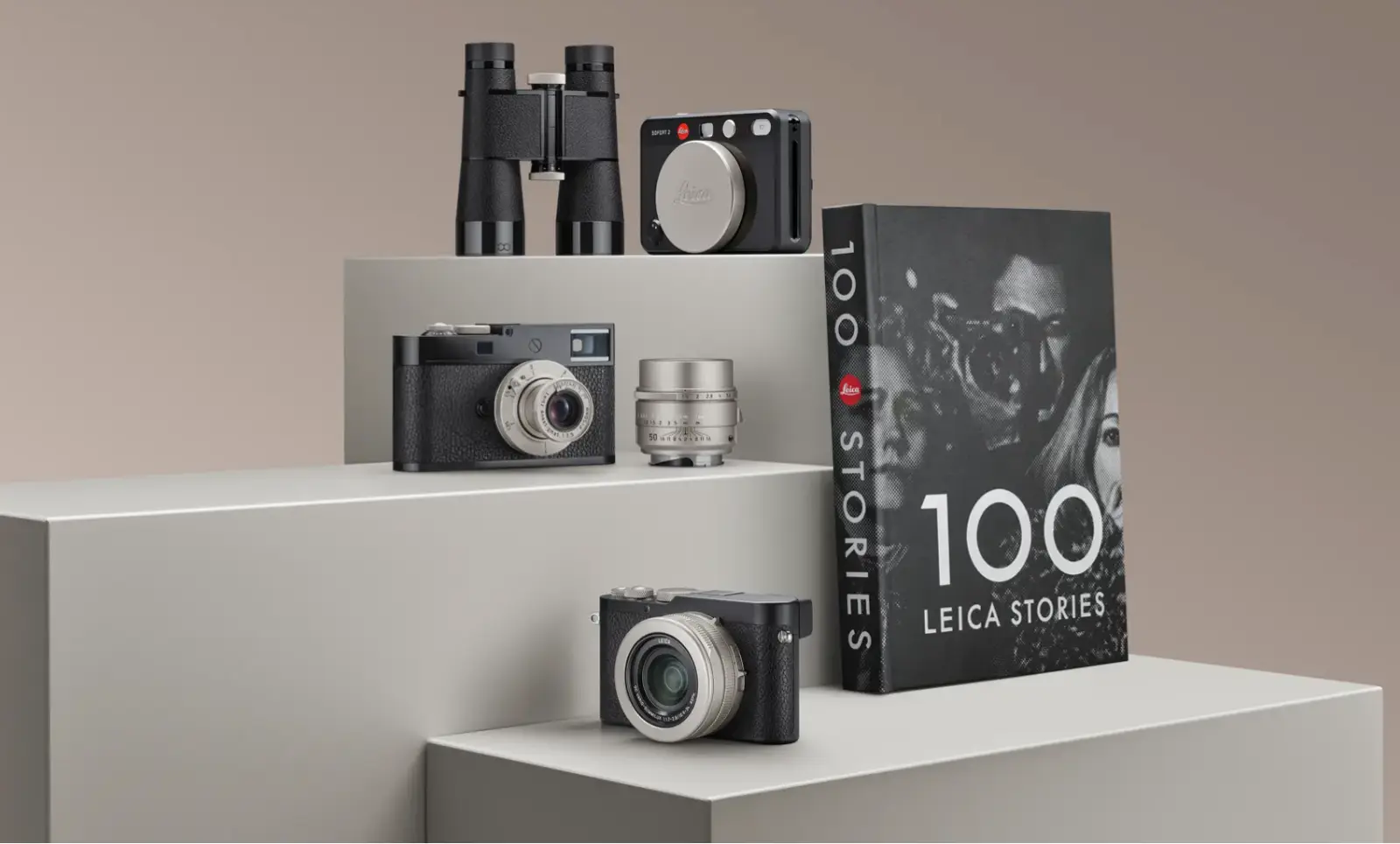 라이카 100주년 기념 스페셜 에디션 제품 단체 사진. M11-D, D-Lux 8, SOFORT 2 카메라와 Trinovid 쌍안경, 그리고 '100 Leica Stories' 사진집이 전시되어 있다.