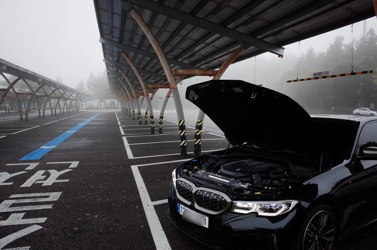 안개 낀 주차장에서 보닛을 열어 엔진룸을 드러낸 검은색 BMW M340i — B58 엔진 순정 상태