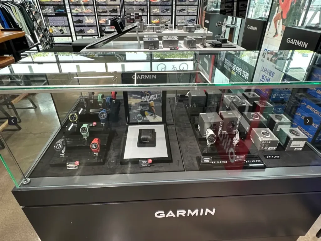 파라마운트 매장 내부의 가민 스마트워치 전시 존. 다양한 색상의 GARMIN 스포츠 워치와 박스 제품이 진열된 유리 진열대 모습