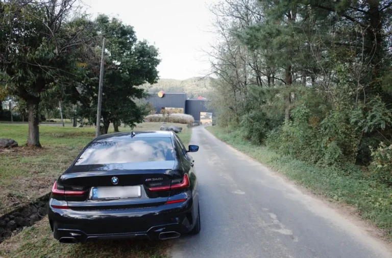BMW M340i가 시골길 끝에 서 있는 모습. 3년간의 오너십 여정을 마무리하며 새로운 길을 바라보는 감성적인 후면샷. 구름 낀 하늘과 자연 풍경이 어우러진 대구 근교 도로