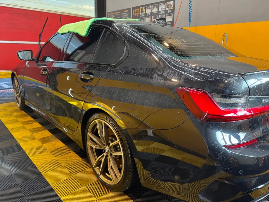 세차장에서 세차 중인 BMW M340i 모습. 물기가 맺힌 차체와 M 스포츠 휠이 선명하게 보이는 장면. M 스포츠 브레이크 분진 관리를 위한 정기적인 세차 과정을 담은 사진