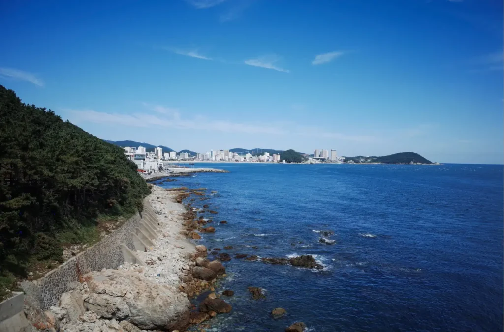부산 청사포 다릿돌 전망대에서 내려다본 넓고 푸른 바다와 해안가의 바위들. 멀리 희미하게 도시의 스카이라인이 보인다.