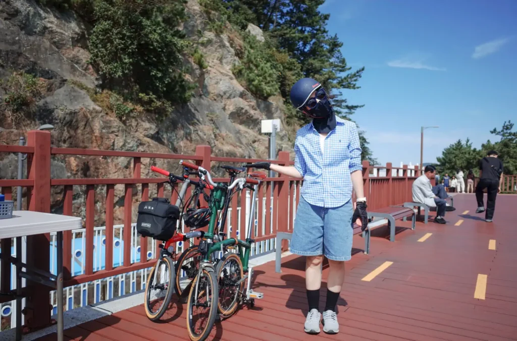 부산 다릿돌 전망대 입구, 운영사무실 옆에 잠시 맡겨둔 브롬톤 CHPT3와 M4L 자전거 옆에 서서 웃고 있는 와이프의 모습