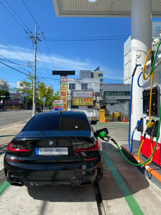 주유소에서 연료를 주입중인 BMW M340i 후면 모습. M340i 엠블럼과 번호판이 선명하게 보이며 주유기의 다양한 연료 옵션들이 표시되어 있음