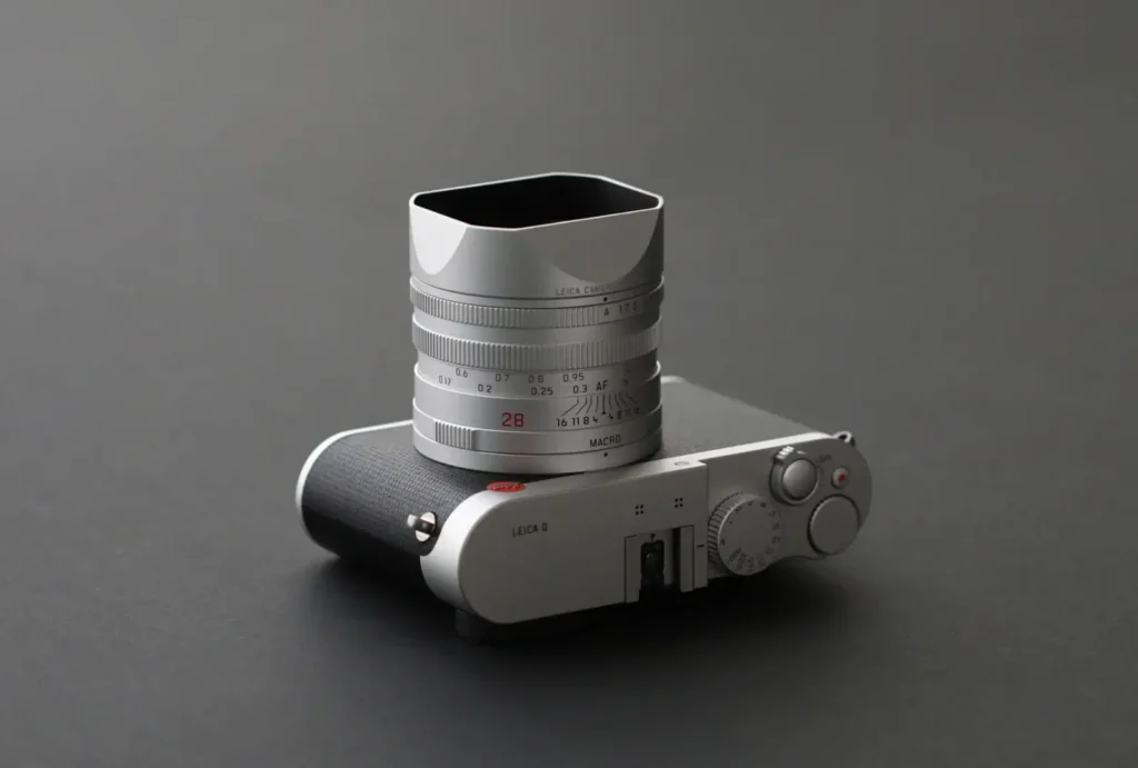 라이카 Q 실버 바디 카메라와 28mm f1.7 렌즈가 회색 배경에 놓여있는 모습