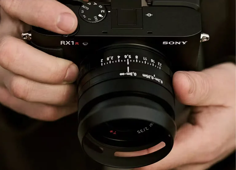 소니 RX1R III 카메라를 두 손으로 감싸 쥐고 있는 모습, 35mm F2 자이스 렌즈와 조리개 링이 선명하게 보이는 프리미엄 컴팩트 풀프레임 카메라