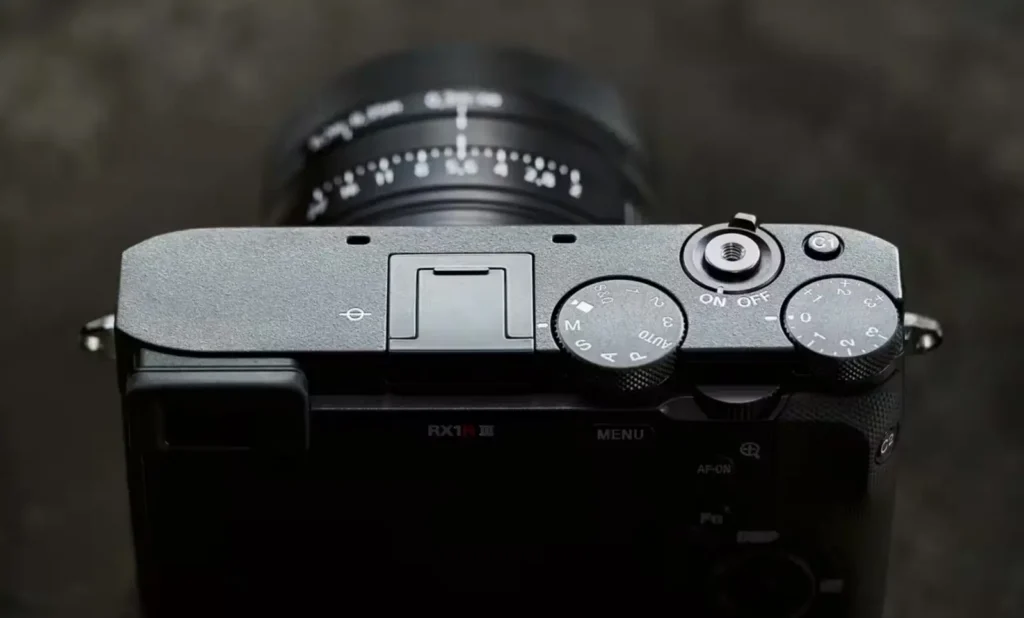 소니 RX1R III 상단부 클로즈업, 평평한 디자인으로 매립된 다이얼과 컨트롤 버튼들, 미니멀한 레이아웃과 RX1R III 로고가 보이는 세련된 상판