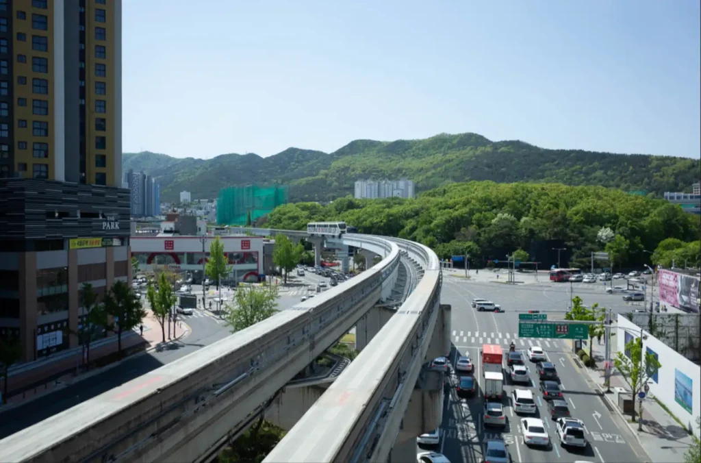 맑은 날 대구 수성못역 근처 두산오거리의 복잡한 도로 위로, 3호선 모노레일 열차가 곡선 선로를 따라 지나가고 있는 도시 풍경.