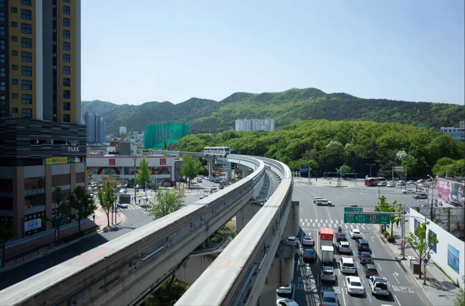 맑은 봄날 대구 수성구 도심에서 내려다본 풍경으로, 3호선 모노레일 선로가 크게 곡선을 그리며 뻗어 있고 선로 위로 열차 한 대가 지나가고 있으며 배경으로 초록 산과 도심 건물들이 어우러져 있다.