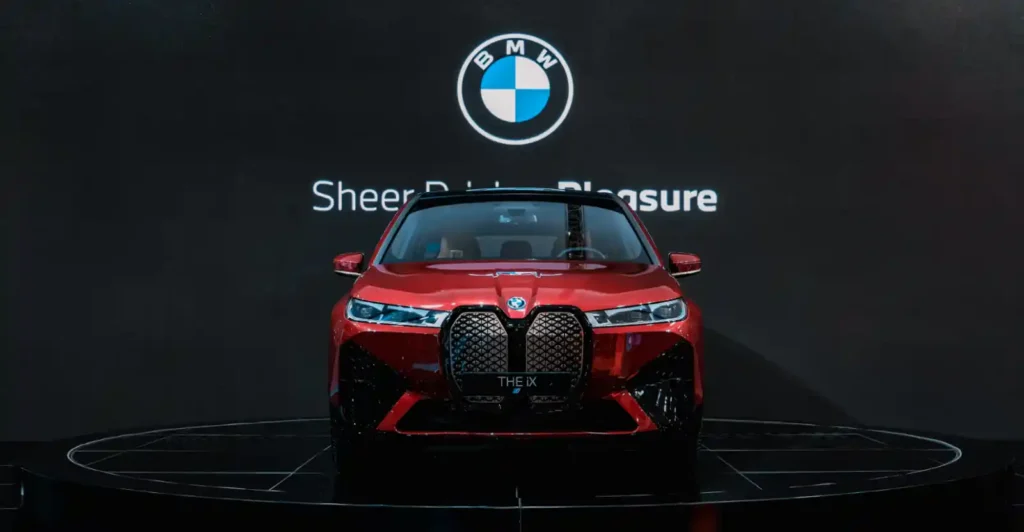 BMW 쇼룸에 전시된 빨간색 BMW iX 전기차. 거대한 키드니 그릴과 슬림한 헤드램프가 강조된 정면 사진입니다.