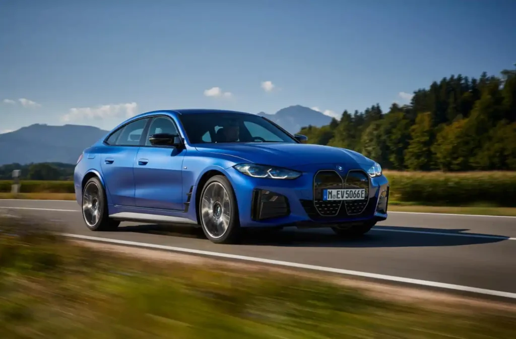 푸른 하늘 아래 구불구불한 도로를 달리는 파란색 BMW i4. 역동적인 주행 사진입니다.