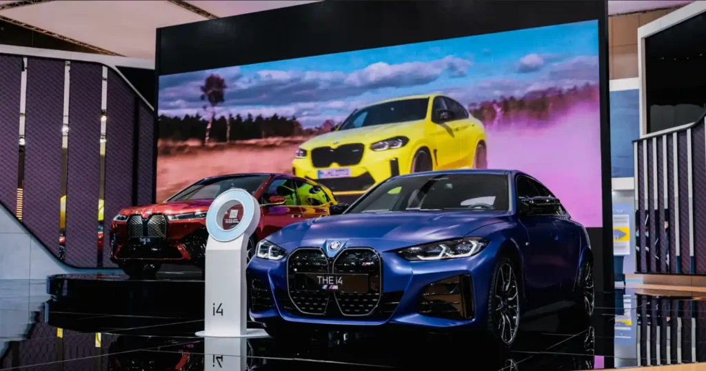 BMW 쇼룸에 나란히 전시된 빨간색 BMW iX와 파란색 BMW i4 전기차. 두 모델의 대비되는 디자인을 정면에서 보여주는 사진입니다.