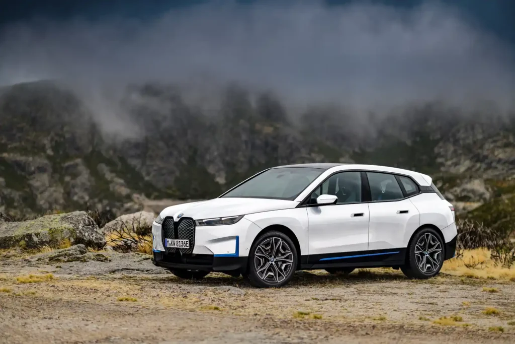 안개가 자욱한 산악 지형에 주차된 흰색 BMW iX. SAV로서의 안정감과 효율성을 강조하는 사진입니다.