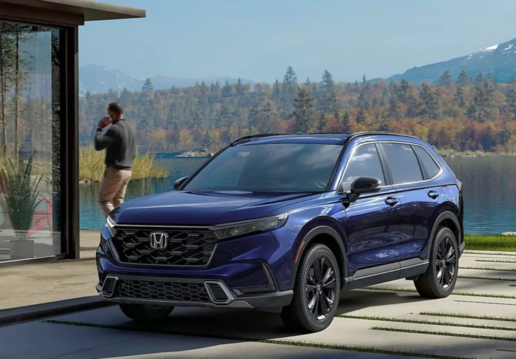 아름다운 호수와 산 배경 앞에 주차된 딥 블루 컬러의 혼다 CR-V 하이브리드와 통화 중인 남성의 모습