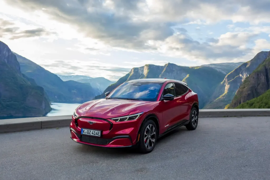 장엄한 피오르드 절벽과 호수를 배경으로 주차된 빨간색 포드 머스탱 Mach-E 전기차