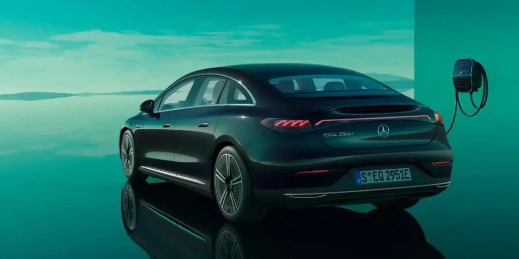 물에 비친 듯한 배경에서 충전 중인 검은색 벤츠 EQE. 전기차의 충전 편의성을 보여주는 사진입니다.