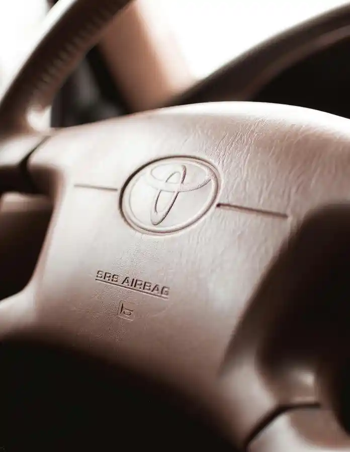 갈색 톤의 자동차 핸들 클로즈업 사진. 중앙에 토요타(TOYOTA) 로고와 SRS AIRBAG 문구가 보인다.