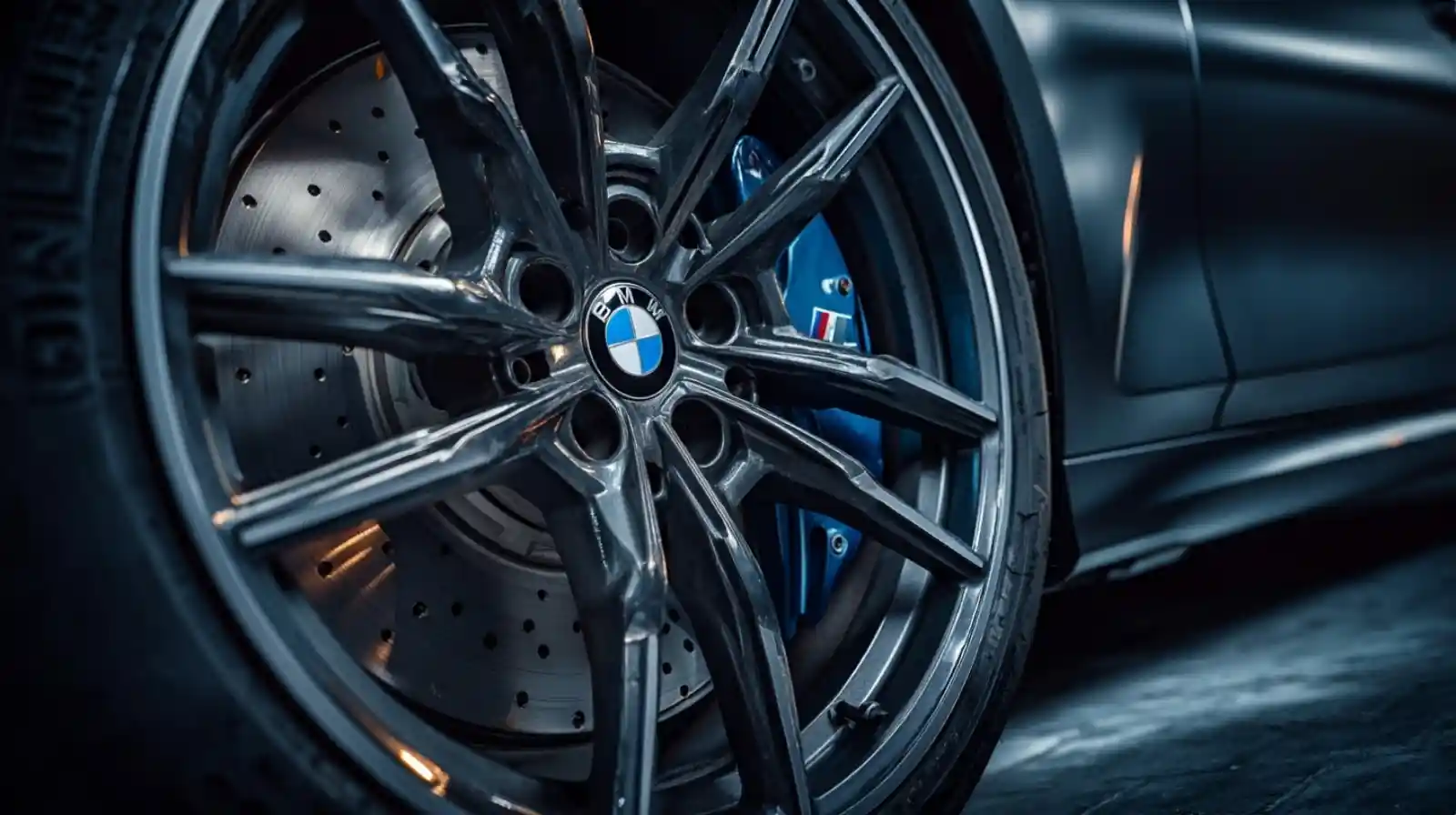 BMW M340i 앞바퀴 클로즈업, M 퍼포먼스 블루 브레이크 캘리퍼와 BMW 로고가 선명한 알로이 휠, 어댑티브 M 서스펜션 시스템이 보이는 전문 자동차 사진