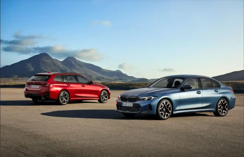 파란색 BMW M340i 세단과 빨간색 M340i 투어링(왜건) 모델이 황량한 평지 위에 나란히 서 있다. 배경으로는 푸른 하늘과 낮은 산들이 보인다.
