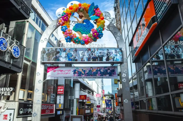 하라주쿠 다케시타 거리 입구의 화려한 컬러풀 풍선 아치와 Takeshita Street 간판, 양쪽 건물 사이로 이어지는 번화한 거리 모습