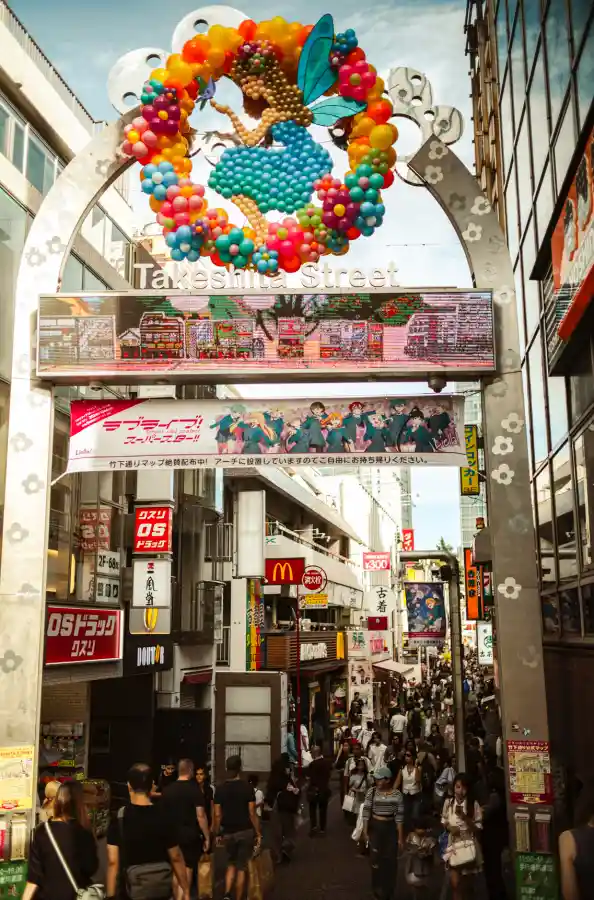 라이카 M10-R로 촬영한 다케시타 거리 전경, 컬러풀한 풍선 아치와 Takeshita Street 간판, 아래로 이어지는 붐비는 거리와 상점들의 세밀한 디테일