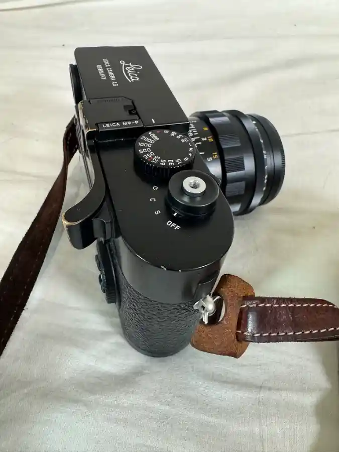 라이카 M9-P 카메라 클로즈업, 검은색 바디에 갈색 가죽 스트랩이 연결되어 있고 렌즈가 장착된 모습