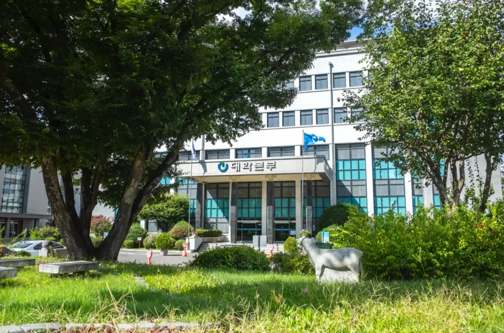 푸른 나무와 잔디밭 사이로 보이는 대구교육대학교 대학본부 건물과 잔디밭 위 작은 동물 조각상