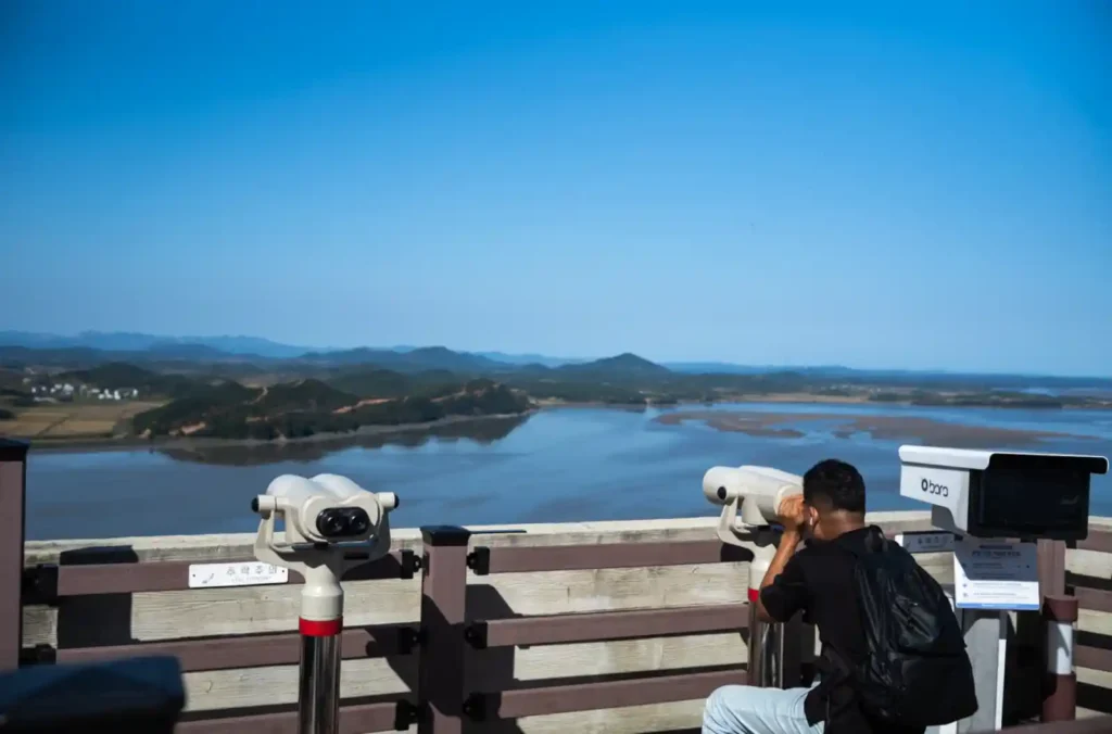 애기봉평화생태공원 전망대 난간에 설치된 망원경을 통해 북한 개풍군 방향을 바라보는 외국인 관광객의 모습. 한강과 임진강이 만나는 지점 너머로 북한의 마을과 산이 보인다.