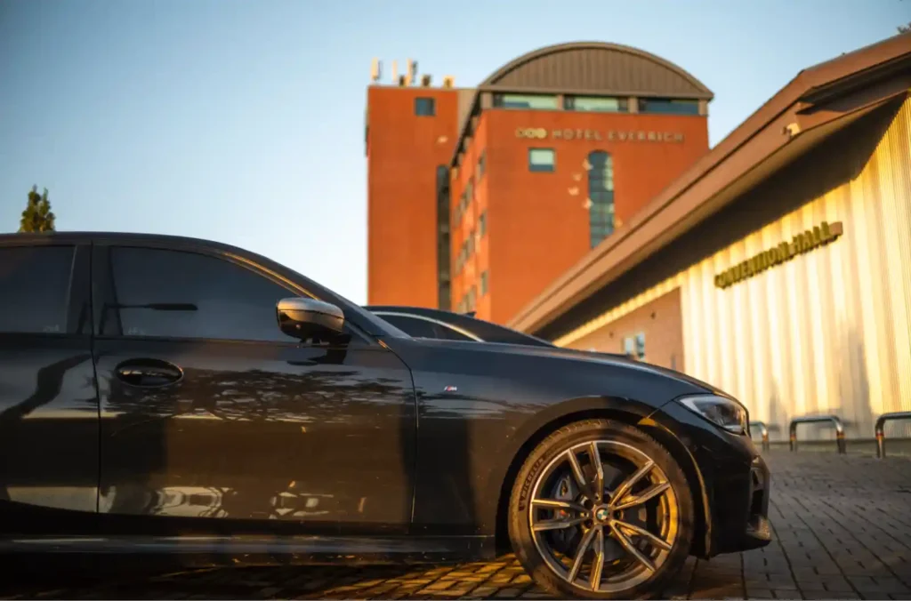 강화 에버리치 호텔 주차장에 주차된 BMW M340i, 아침 햇살에 반짝이는 검은 차체와 주황색 호텔 건물의 강렬한 대비