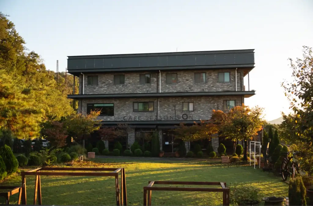강화 에버리치 호텔 별관, CAFE SEASONS ON 회색 벽돌 건물과 아침 햇살이 비추는 정원 잔디밭 전경