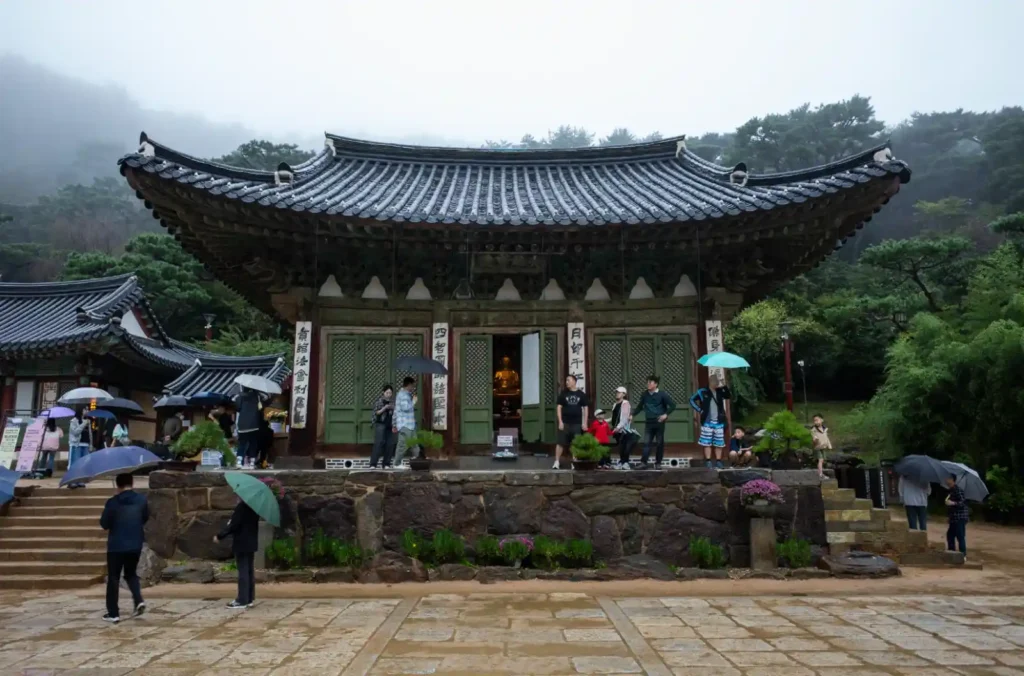 리코 GR2로 촬영한 강화도 전등사 대웅보전의 정면 전경, 빗물에 젖은 기와지붕과 기단, 우산을 든 방문객들