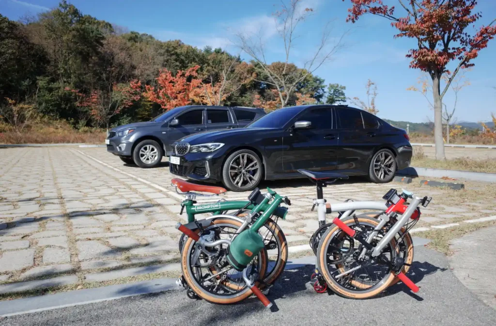 상주 자전거박물관 주차장에 세워둔 자동차 앞에 접어둔 브롬톤 두 대가 놓여 있습니다. 가을 햇살 아래 출발을 준비하는 순간이 담긴 모습입니다.