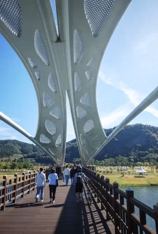 상주 경천섬으로 이어지는 범월교 위를 사람들과 자전거가 함께 건너고 있습니다. 브롬톤을 끌며 걷는 라이더의 모습과 독특한 다리 구조가 인상적입니다.