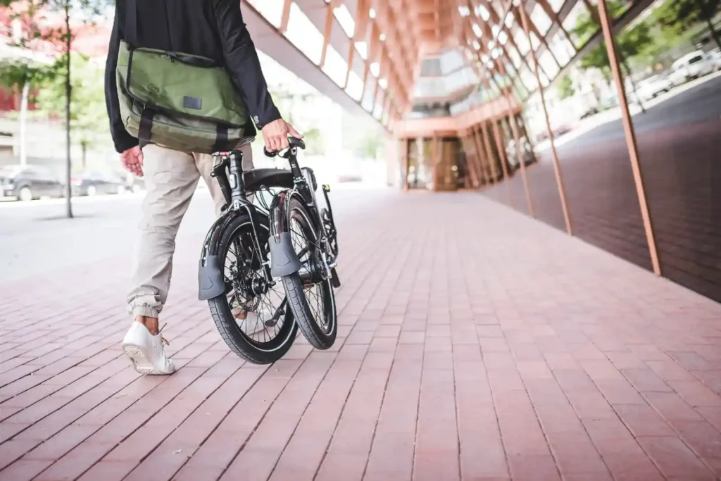 접힌 Tern 폴딩바이크를 끌고 도심 거리를 걷는 라이더 — 매일 타는 사람을 위한 실용적 설계와 Rider First 철학을 상징하는 장면