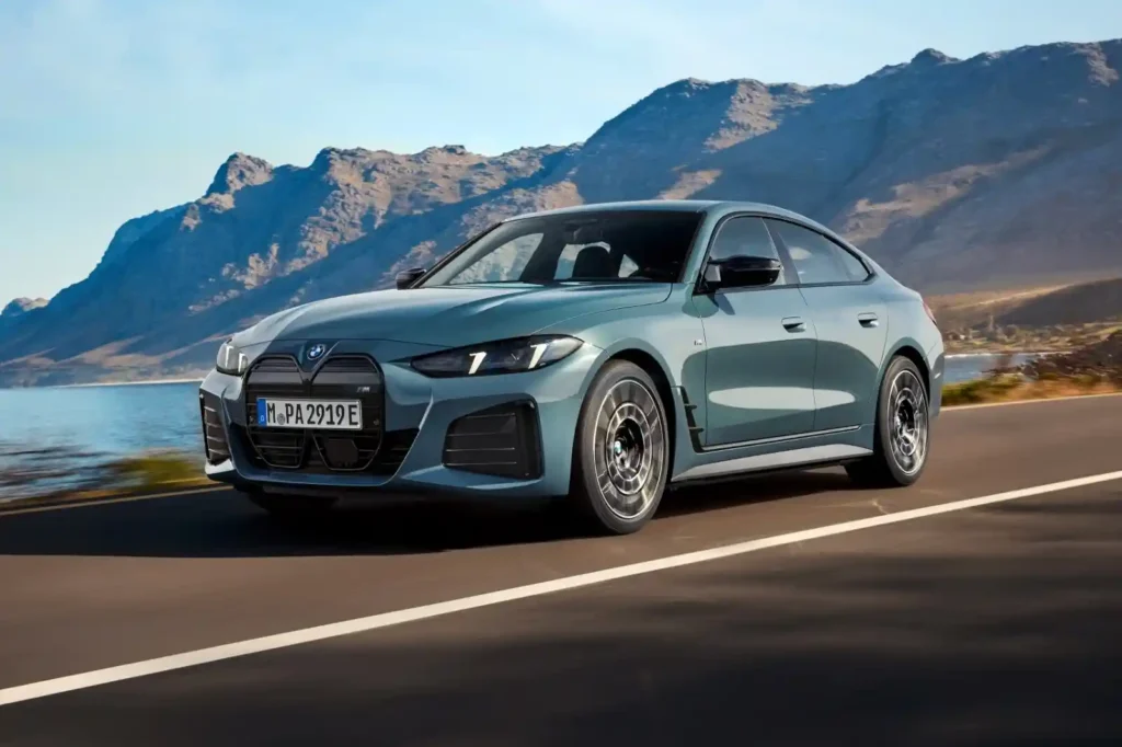 BMW i4 전기 그란 쿠페가 해안 도로를 주행하는 모습으로, 슬림한 헤드램프와 고성능 디자인 요소가 강조된 주행 이미지.