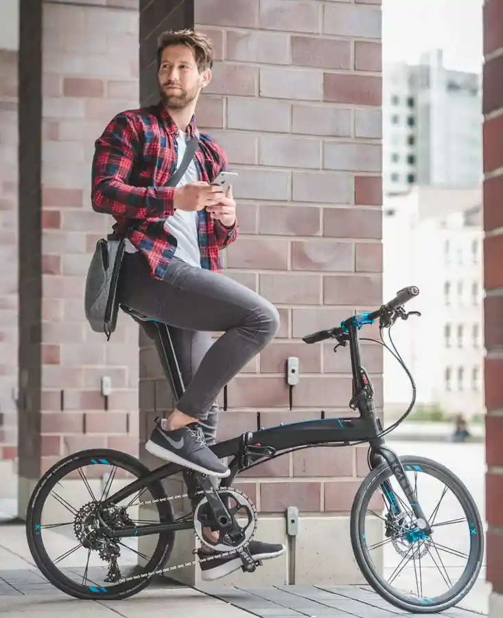 도심 건물 앞에서 턴 폴딩자전거에 앉아 휴대폰을 들고 있는 남성, 도시 라이프스타일 속 폴딩바이크 장면