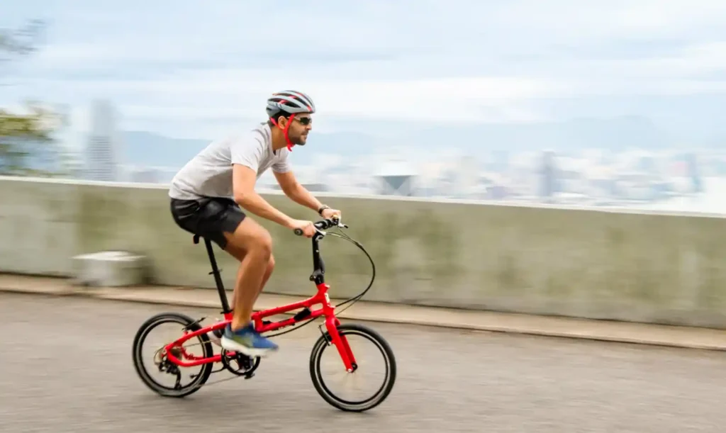 빨간색 턴 BYB 폴딩자전거를 탄 남성이 도심 도로를 달리고 있습니다. 알루미늄 프레임의 가벼움과 즉각적인 반응성을 보여주는 장면입니다.
