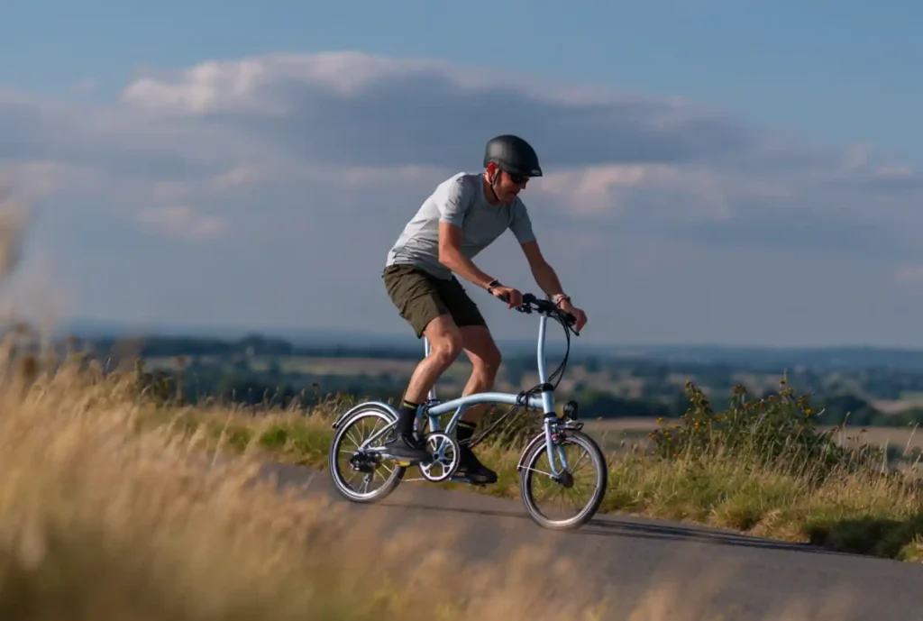 브롬톤 폴딩자전거로 언덕길을 오르는 라이더, 황금빛 들판 배경