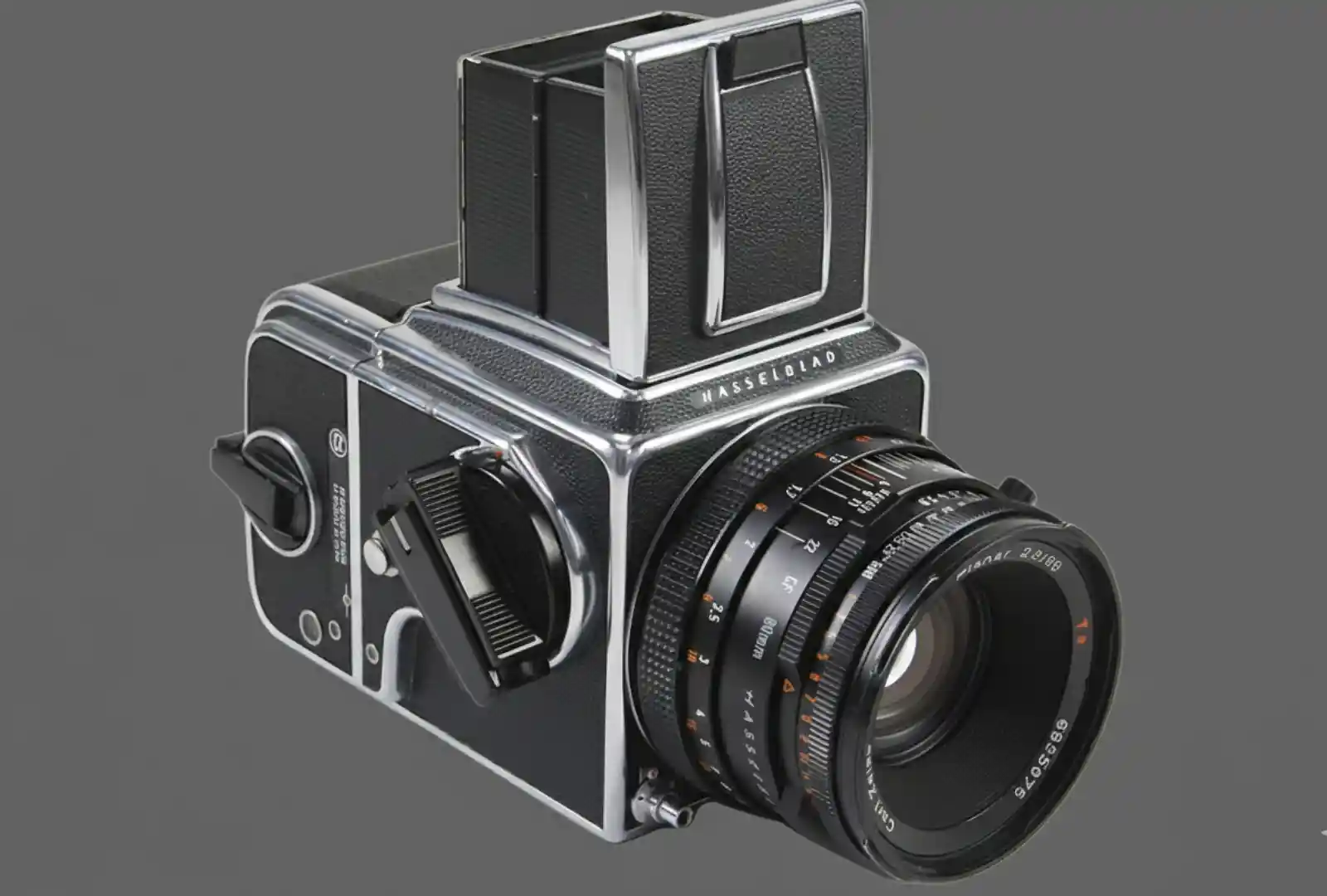 Hasselblad V 시스템 필름 카메라가 차콜 배경 위에 놓여 있는 모습. 금속 바디와 칼 자이스 렌즈가 선명하게 보이는 중형 포맷 카메라 클로즈업