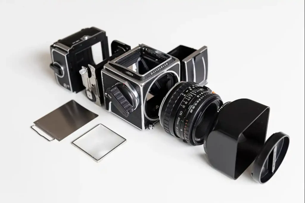 핫셀블라드 V 시스템 카메라가 바디, 렌즈, 필름백, 파인더, 다크 슬라이드 등으로 분해된 상태로 흰색 배경 위에 가지런히 놓여 있는 모습.