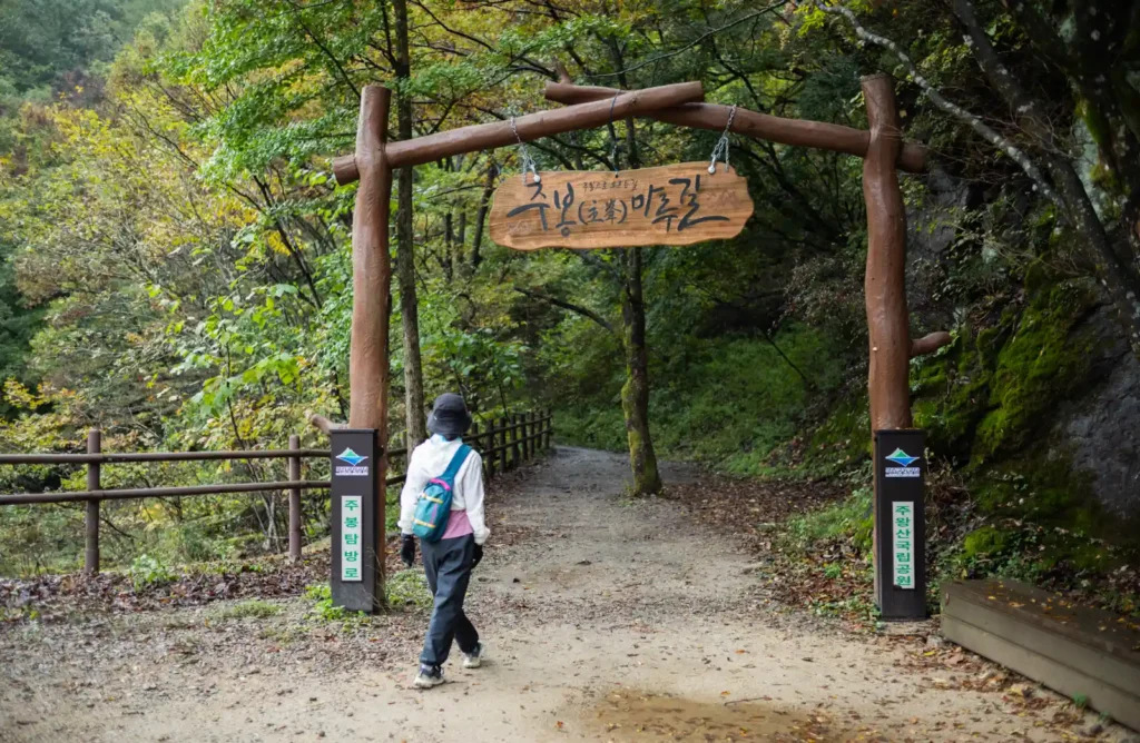 주왕산 주봉 탐방로 입구 나무 간판 아래를 지나는 등산객