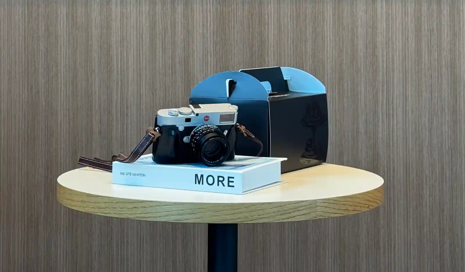 Leica M10-R과 Summilux 35mm f/1.4 II 렌즈가 책 위에 놓여 있는 모습. 나무 테이블과 부드러운 조명 아래, 조용한 분위기의 정물 구도.